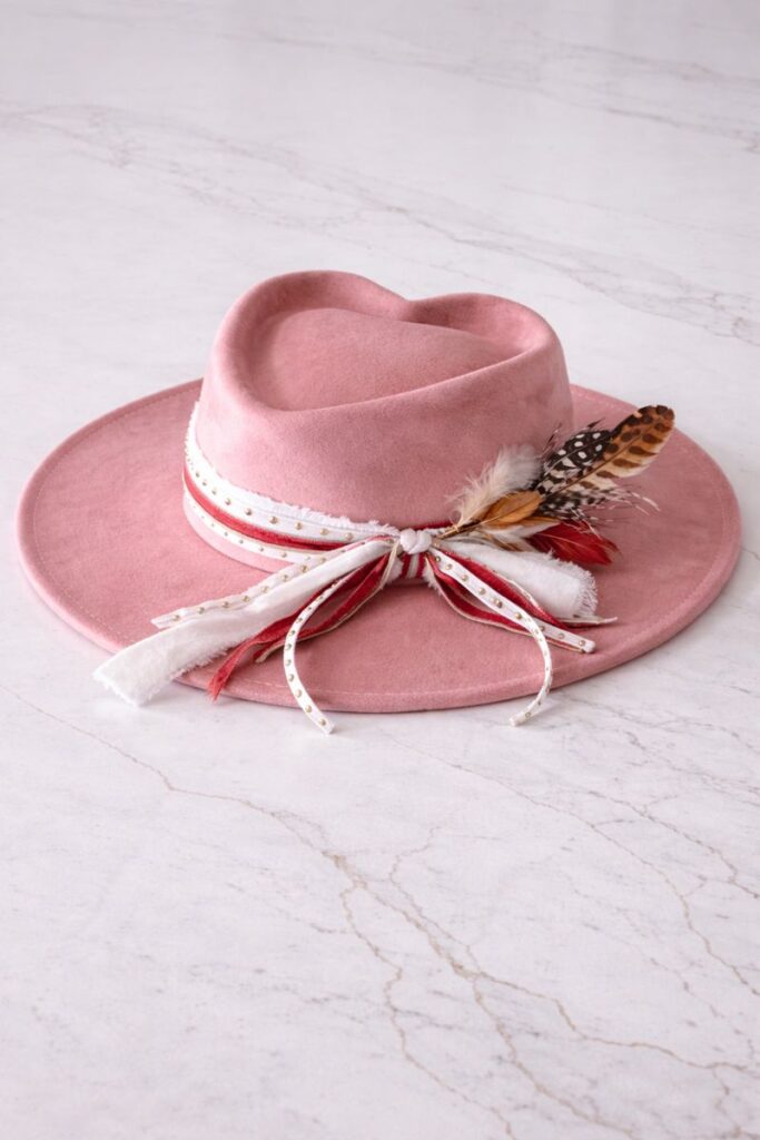 Dusty rose heart-crown vegan suede hat with ribbon band, gold stud details, and feather accent by Swanky Doodle Boutique & Hat Bar in Fort Worth, Texas.