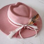 Flat brim dusty rose heart-crown hat featuring layered red and white ribbons and feather detail, photographed for Swanky Doodle Boutique & Hat Bar in Fort Worth, TX.