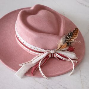 Flat brim dusty rose heart-crown hat featuring layered red and white ribbons and feather detail, photographed for Swanky Doodle Boutique & Hat Bar in Fort Worth, TX.