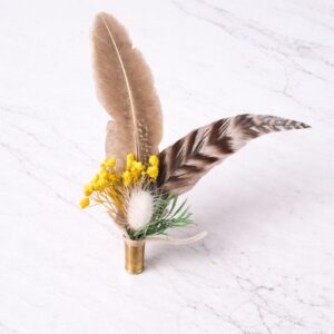 Feather and dried flower hat accent in a brass casing on white marble, Swanky Doodle Boutique inside Painted Tree in North Richland Hills, TX near Fort Worth.