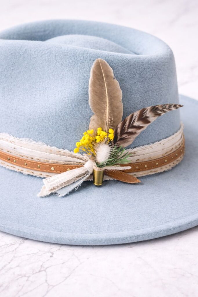 Feather and dried flower hat accent in a brass casing, available at Swanky Doodle Boutique & Hat Bar near Fort Worth, TX inside Painted Tree North Richland Hills.