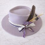Lilac wool felt rancher pinch front hat styled with purple and white ribbons, “Game Day” patch, and feather accents by Swanky Doodle.