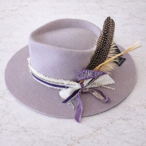 Lilac wool felt rancher pinch front hat styled with purple and white ribbons, “Game Day” patch, and feather accents by Swanky Doodle.